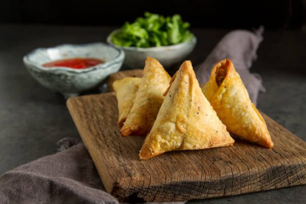 Asian food. Vegetarian samsa with tomato sauce and herbs. Dark background